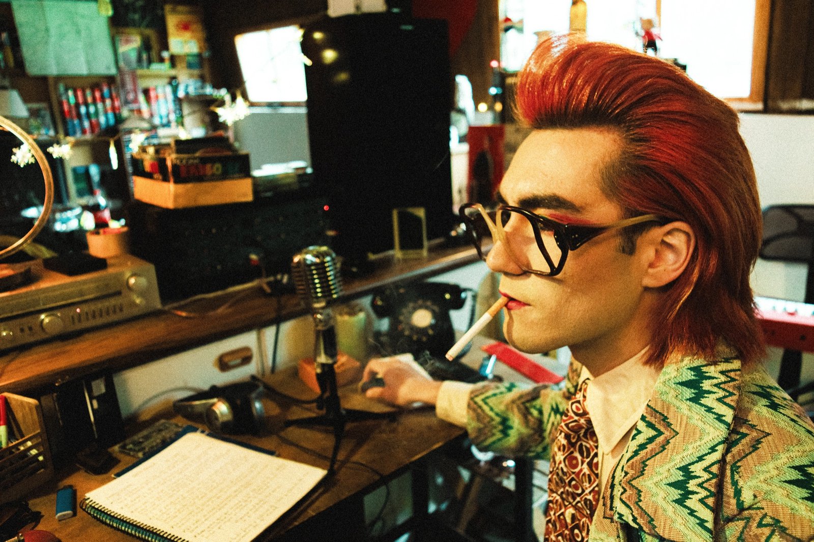 Gaspar Luna al micrófono vintage con chaqueta de zigzag verde, cigarrillo y gafas de pasta